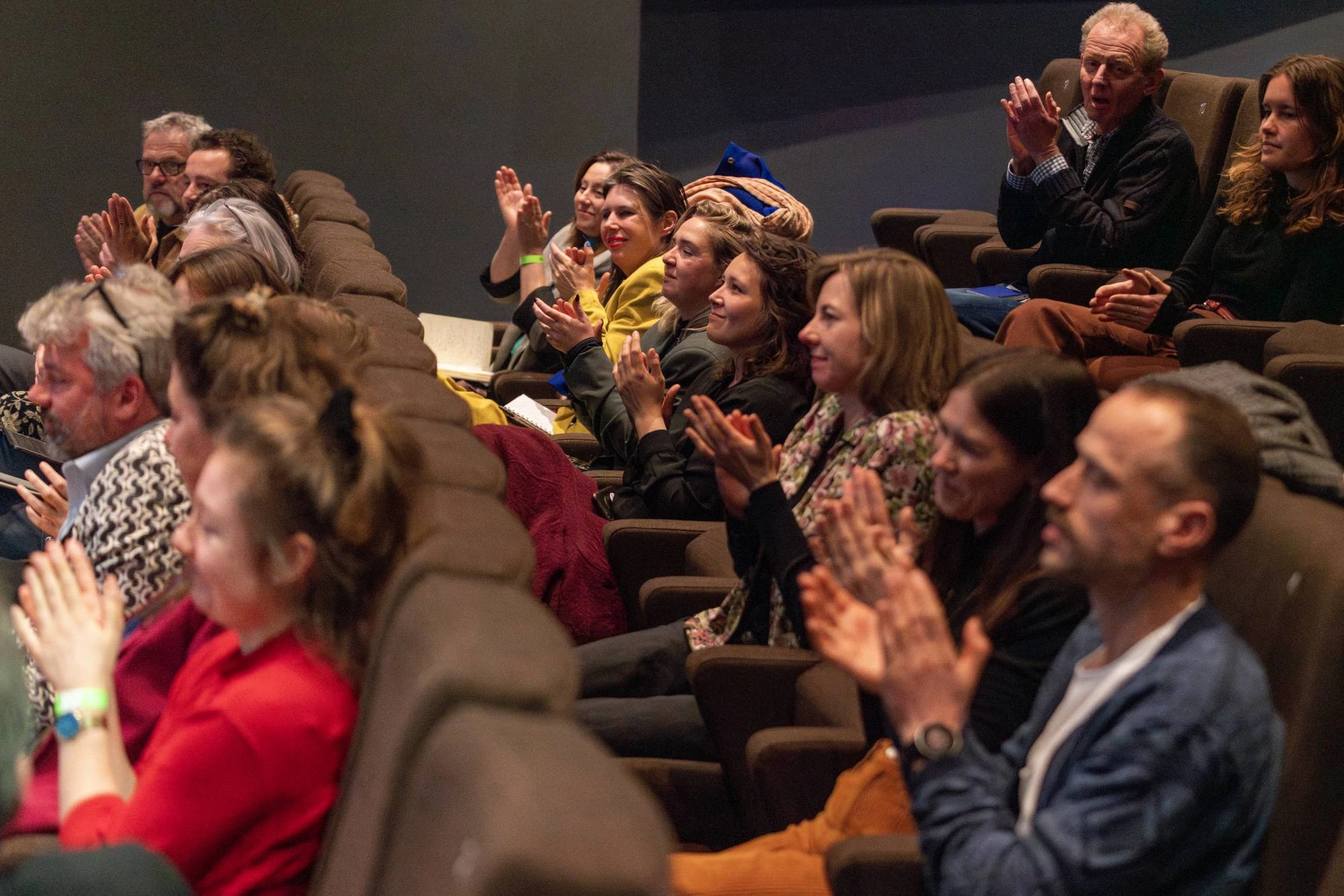 Een groep mensen in een zaal klapt enthousiast tijdens een presentatie of voorstelling. De sfeer is positief en betrokken
